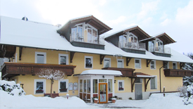 Unser Haus im winterlichen Bayerischen Wald - ein gelb gestrichenes, freundliches Gebäude mit zahlreichen Balkonen